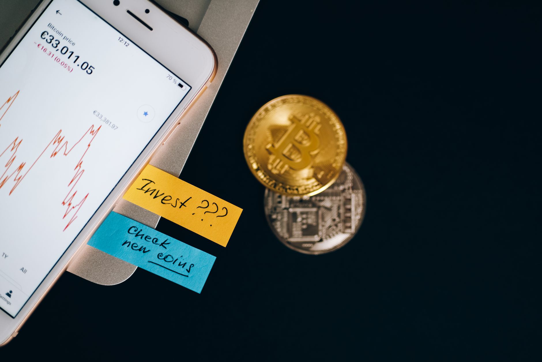 Smartphone displaying a crypto trading chart next to physical coins on a desk