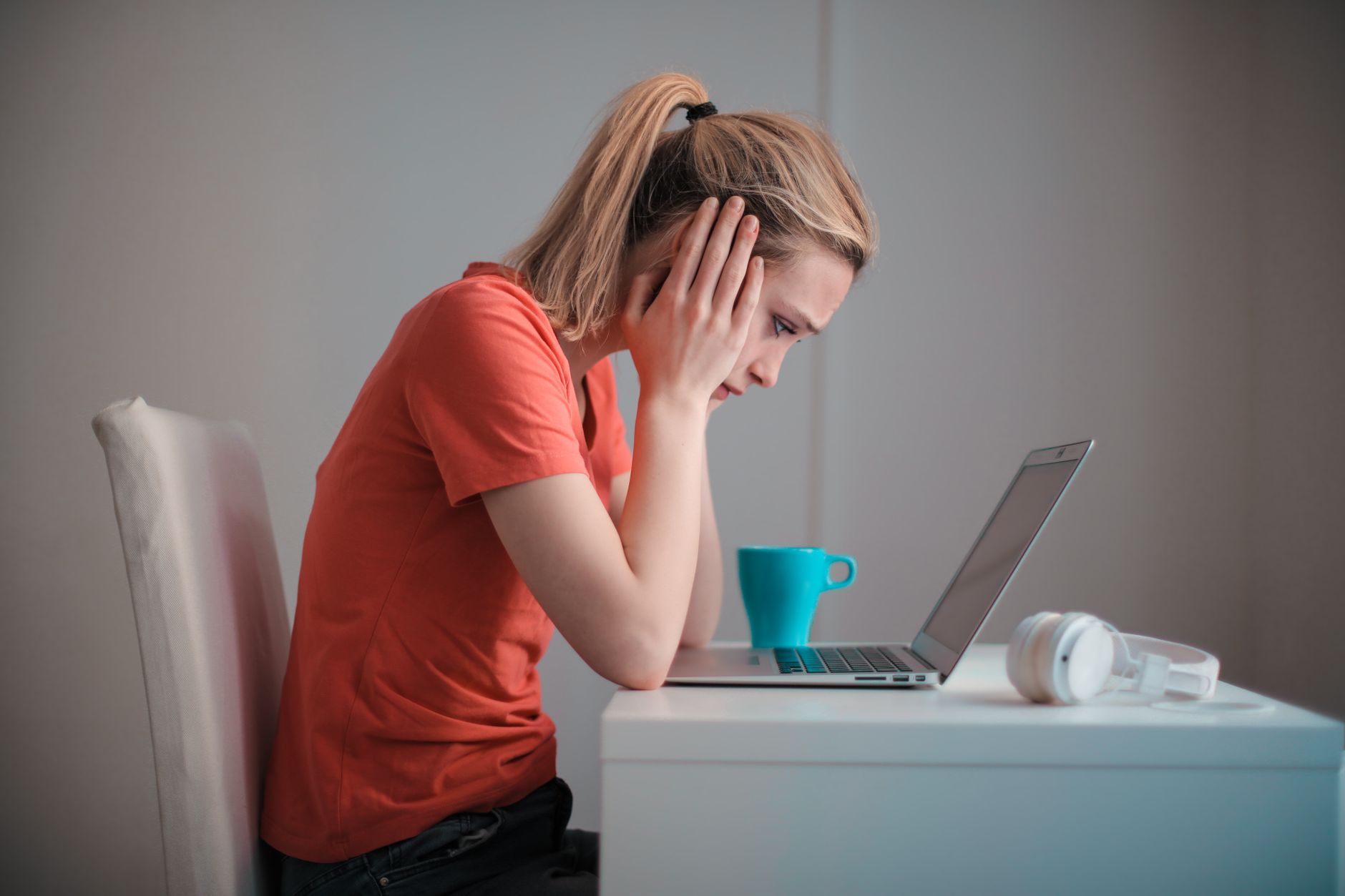 A person wearing headphones stares at a laptop screen with a concerned expression in a home office.