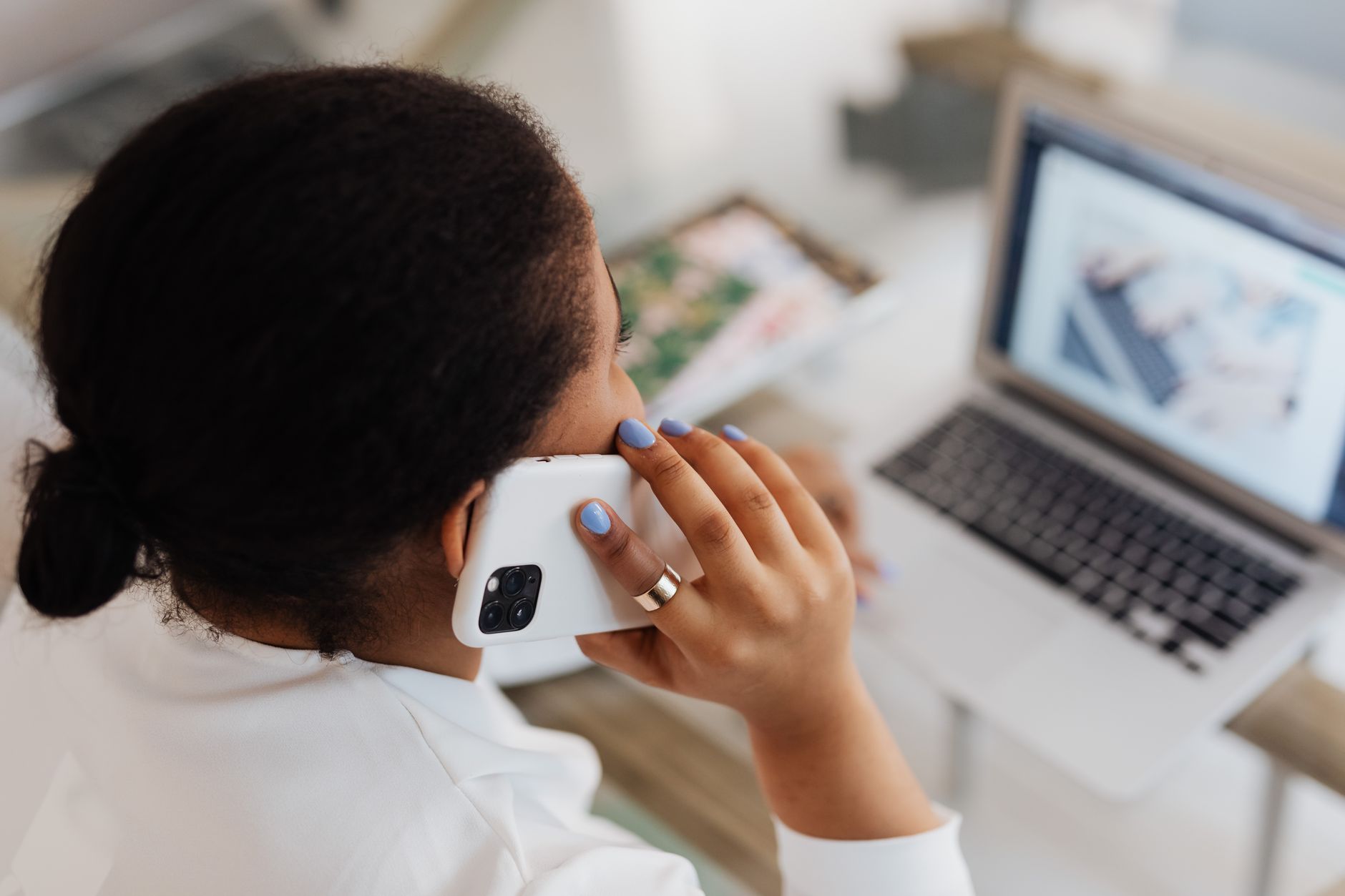 A person speaks on the phone while looking at a credit report on a laptop at a home desk.
