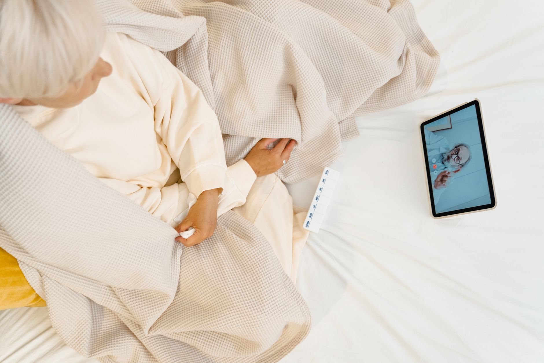 An older woman looks confused while watching a video call on a tablet with a person on the screen.