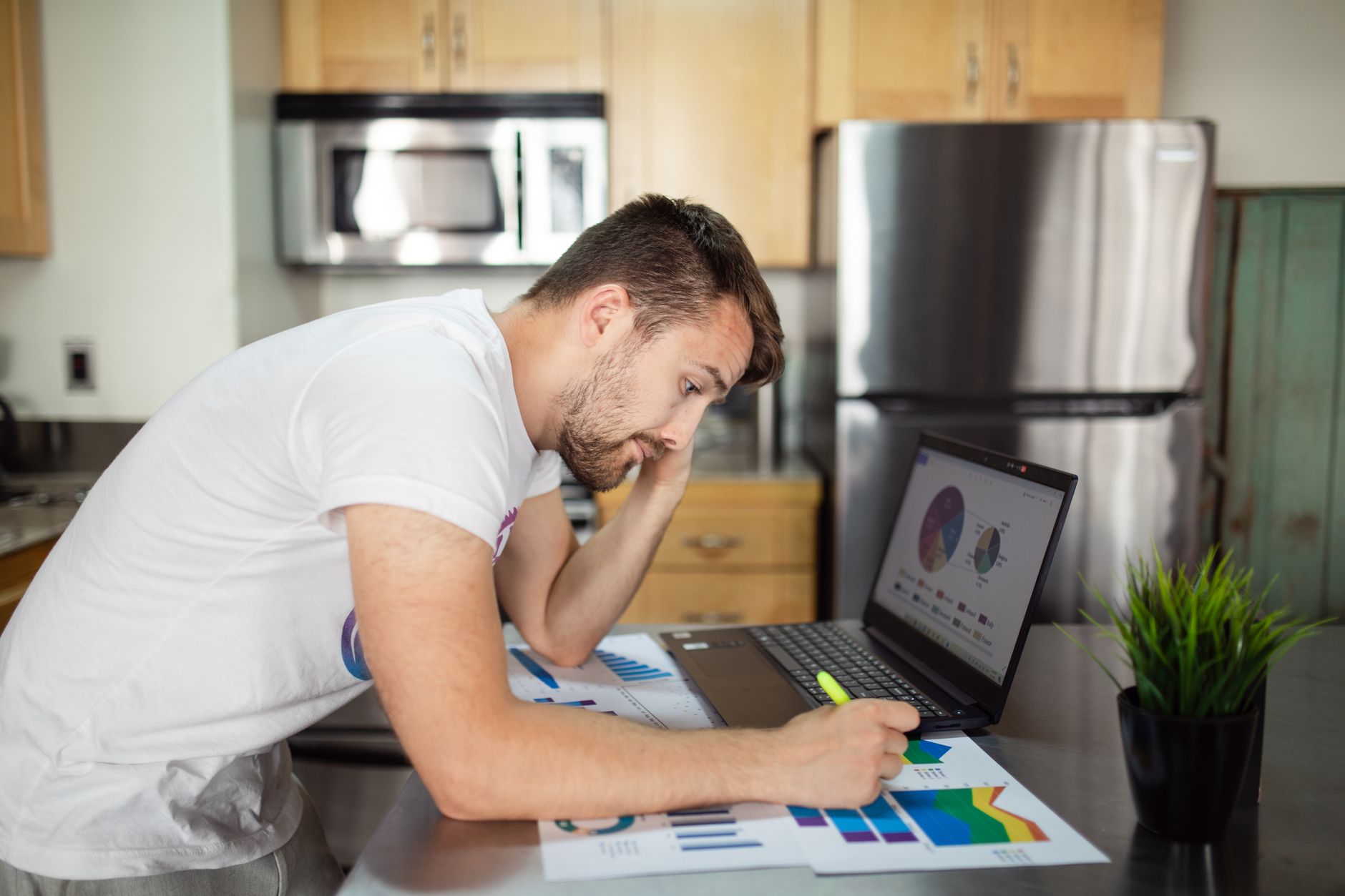A person at a kitchen table reviews a credit report on a laptop with a concerned expression