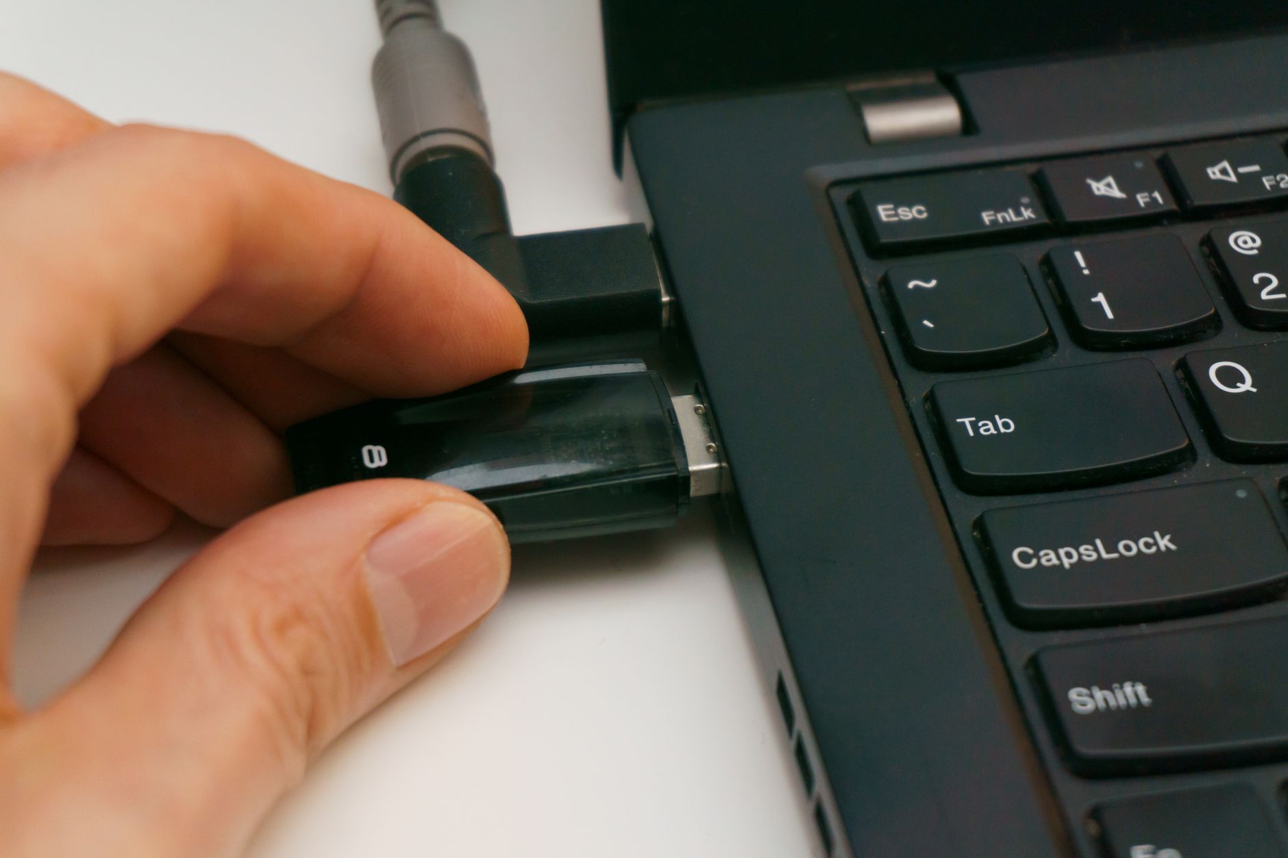 A hardware security key inserted into a laptop USB port with a hand tapping it.